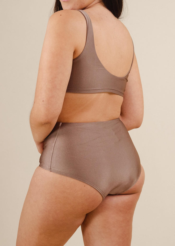 A woman in beige high waist bikini bottoms with very good coverage.