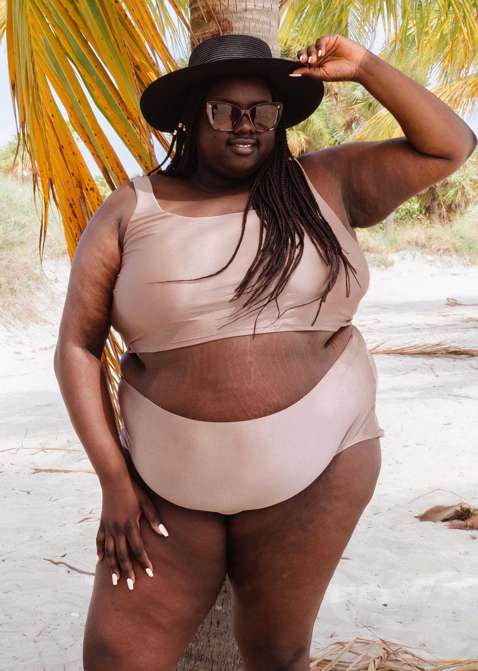 Une femme vêtue d'un bas de bikini taille haute Mimi et August Paloma Dunes et d'un chapeau pose pour une photo.