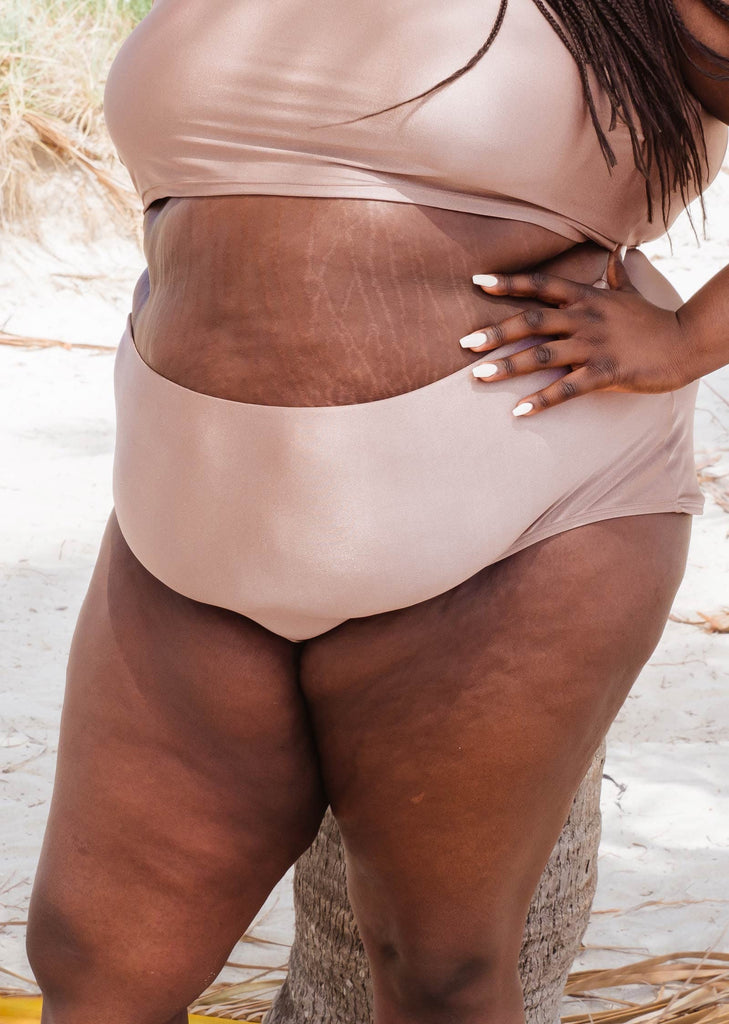 Gros plan sur un bas de bikini de couleur beige sable porté par une femme debout sur la plage de Miami.