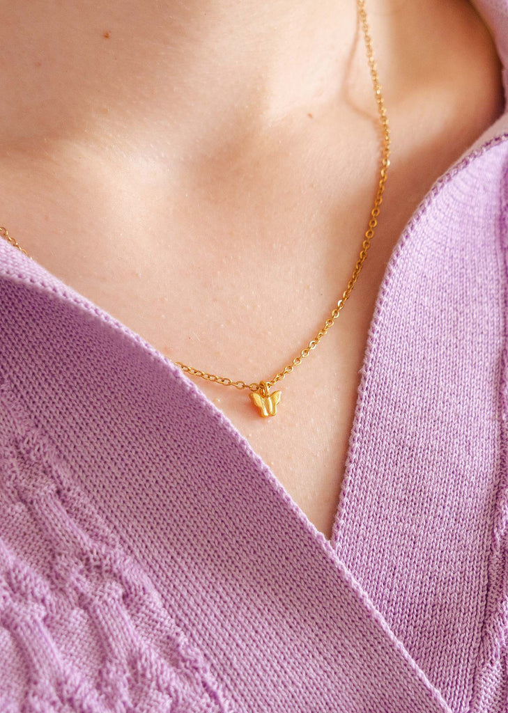 A close up of a person wearing a Mimi and August Papillon gold plated necklace.