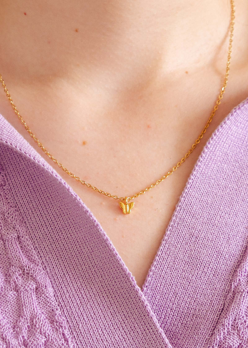 A close up of a person wearing a mimi and august gold plated butterfly necklace.