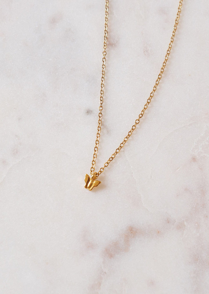 A Mimi and August papillon gold plated necklace on a marble surface.