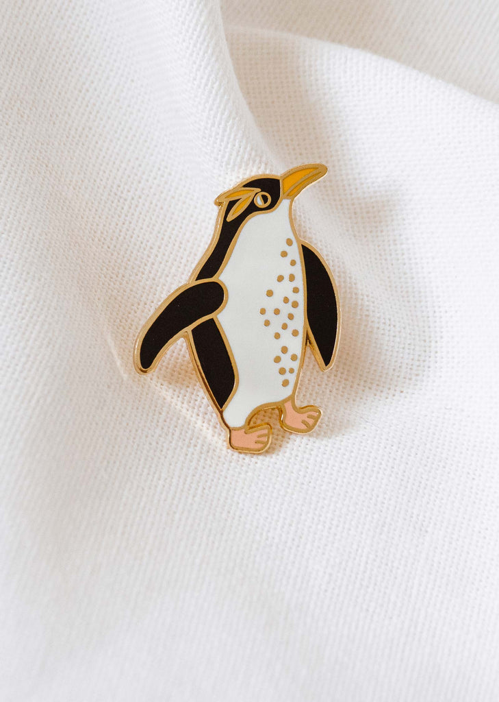 A winter-themed penguin enamel pin by mimi and august on a white shirt