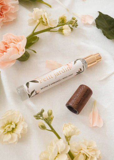 A close up of mimi and august room spray 10ml tube next to blooming flowers.