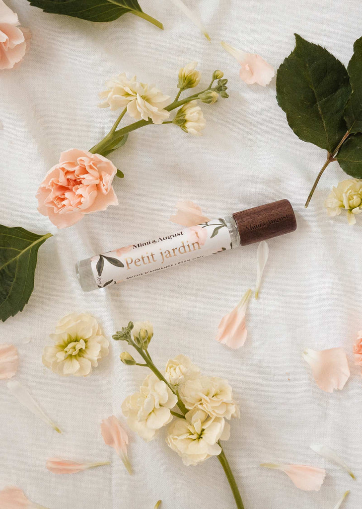 A bottle of mimi and august Flower room spray surrounded by flowers