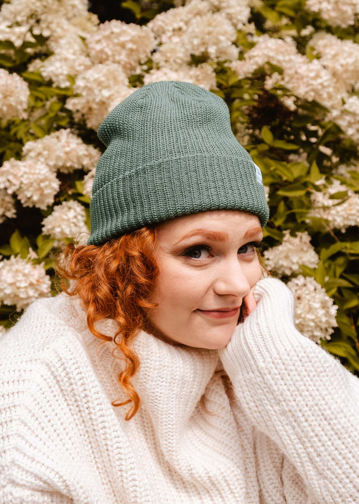 A woman wearing a Pistachio Cuffed Beanie posing in front of flowers.
