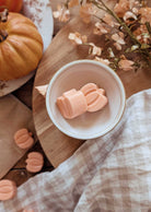 A white bowl holds two pumpkin-shaped candies on wood, surrounded by a small pumpkin and dried flowers—ideal for highlighting Mimi & August’s Free Pumpkin Wax Melts (100% off) offer.