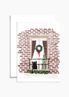 The "Purr-fectly Waiting for Santa - Christmas Greeting Card" by Mimi & August beautifully depicts a black cat on a balcony with a brick wall backdrop, a Christmas wreath on the window, and an indoor festive tree—the perfect scene for holiday cards printed on recycled paper.