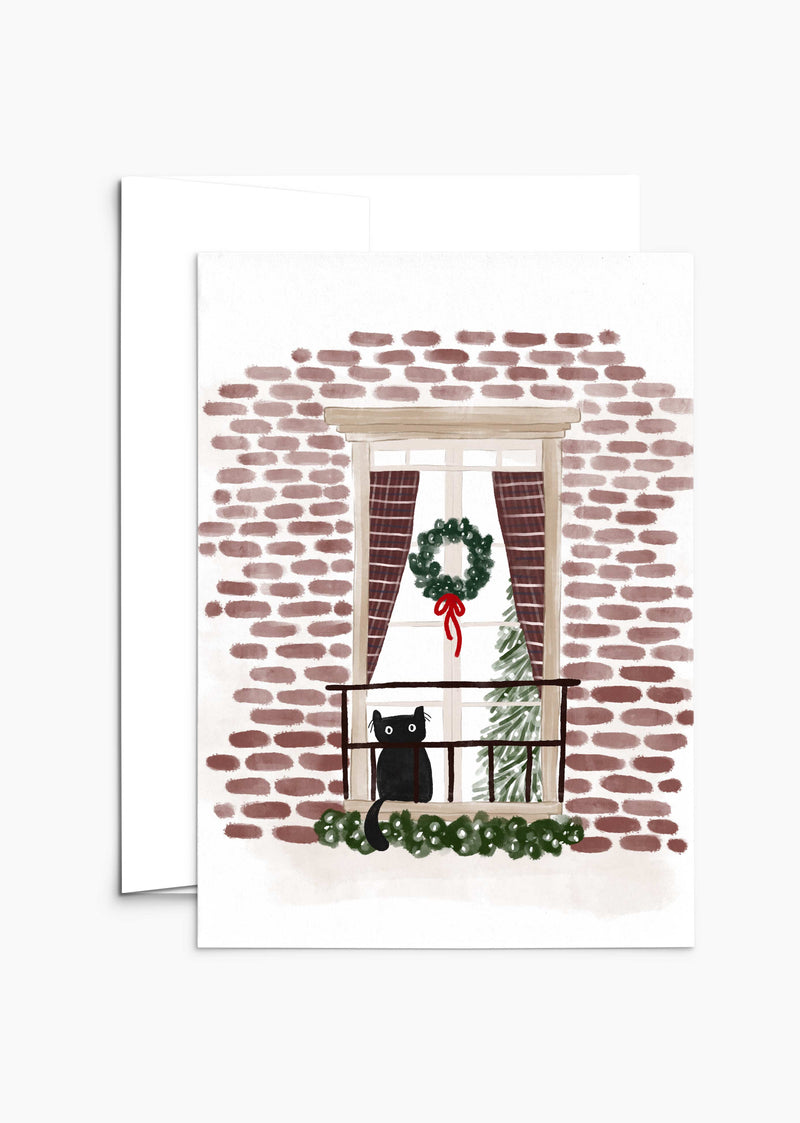 The "Purr-fectly Waiting for Santa - Christmas Greeting Card" by Mimi & August beautifully depicts a black cat on a balcony with a brick wall backdrop, a Christmas wreath on the window, and an indoor festive tree—the perfect scene for holiday cards printed on recycled paper.