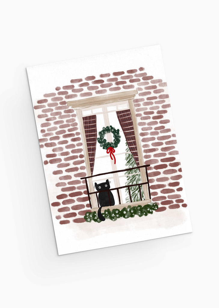 Purr-fectly Waiting for Santa - Christmas Greeting Card by Mimi & August features a charming illustration of a black cat perched on a balcony railing, surrounded by festive elements like a wreath and red curtains against a brick wall. Inside the window, a twinkling Christmas tree adds to the holiday spirit. This beautifully designed card is made with recycled paper and packaged in compostable materials.