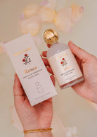 A person holds the Mimi & August Room Spray - Rosea, a citrus floral scent with minimalist floral designs and gold accents—ideal for enhancing any home fragrance collection.