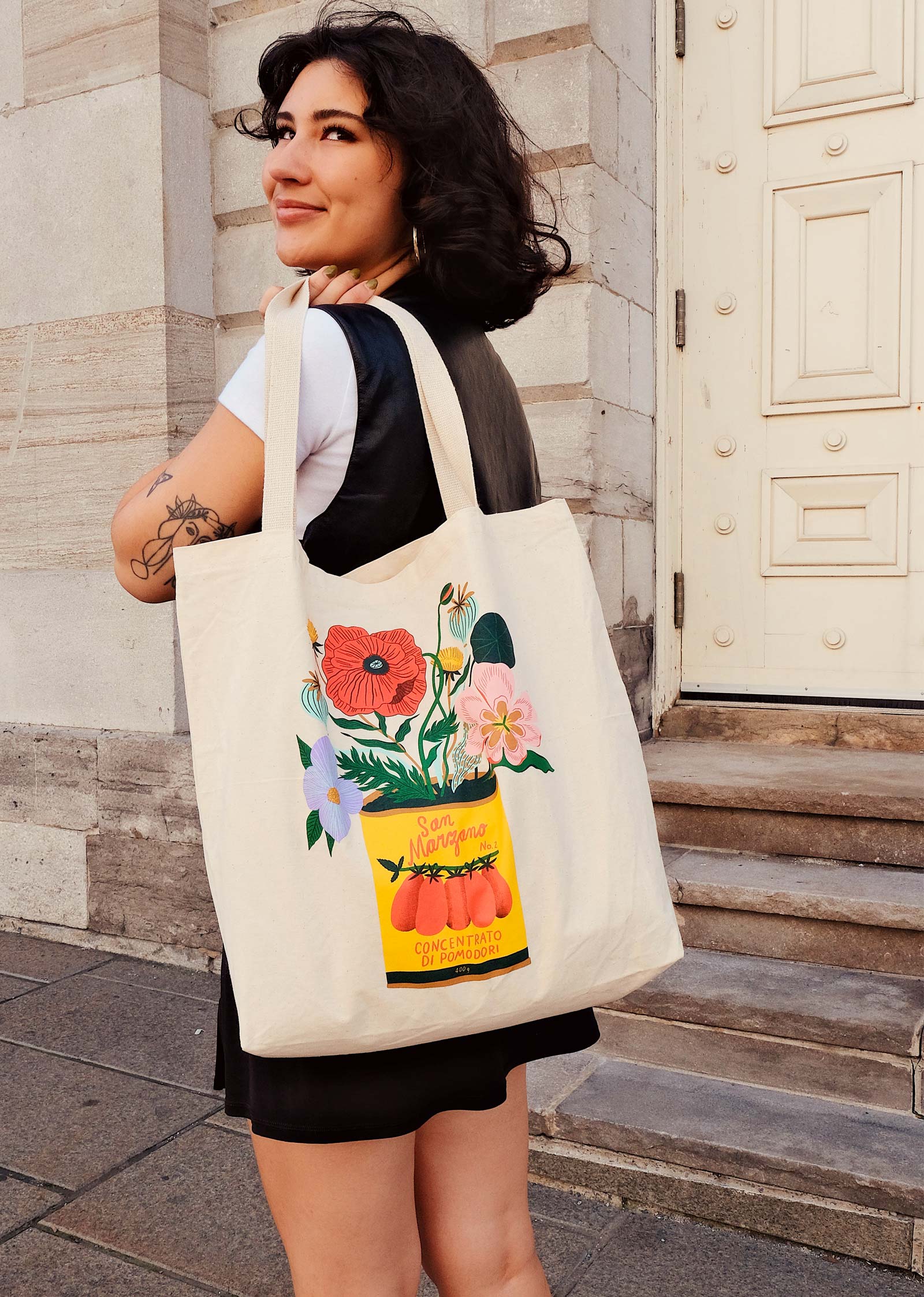 Une femme tenant un sac fourre-tout mimi et august avec des une illustration d'une canne de tomate avec des fleurs