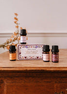 Le Coffret découverte d'huiles à diffuser de Mimi & August, présentant quatre petites bouteilles dans une boîte étiquetée, est exposé sur une surface en bois avec des fleurs séchées en arrière-plan.