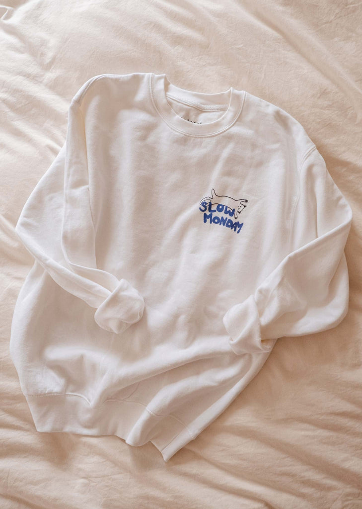A cozy white Slow Monday Sweatshirt from Mimi & August is gently laid atop a bed.