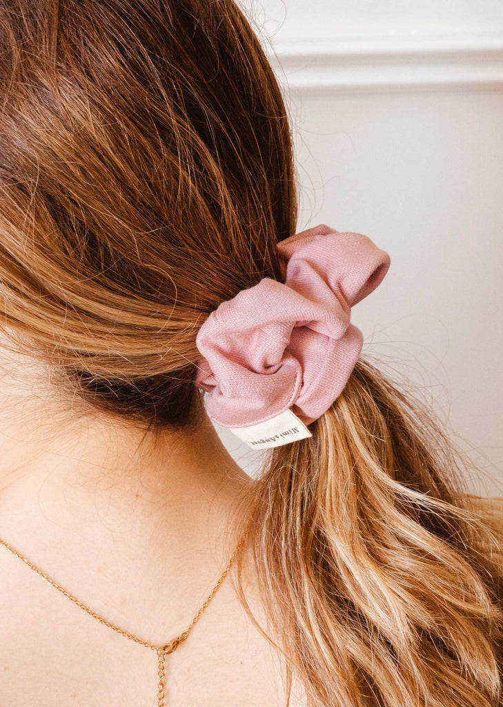 A woman wearing a color soft pink scrunchie by mimi and august.
