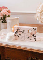 A box labeled "Mimi & August" is on a marble surface beside three Musea soy wax melts, with flowers and a white ceramic warmer in the background.