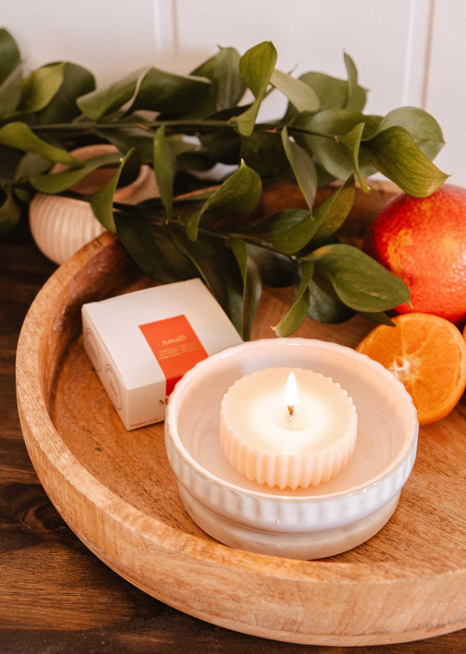 The Mimi & August Candle Refill - Amalfi, displayed with a white dish, box, leafy greens, and citrus on a wooden tray, brings fresh Mediterranean fragrance to your space.