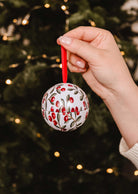 A hand holds the Mimi & August Spiced Cranberries - Christmas Ornament Candle, adorned with red berries, green leaves, and a red ribbon—the perfect festive bauble to fill your home with a warm spiced cranberry scent.