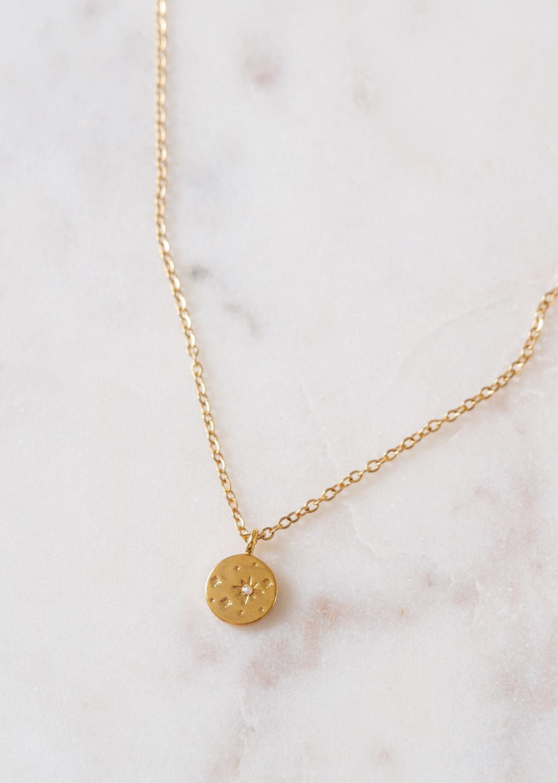 A Mimi and August stellar constellation gold plated necklace on a marble surface.