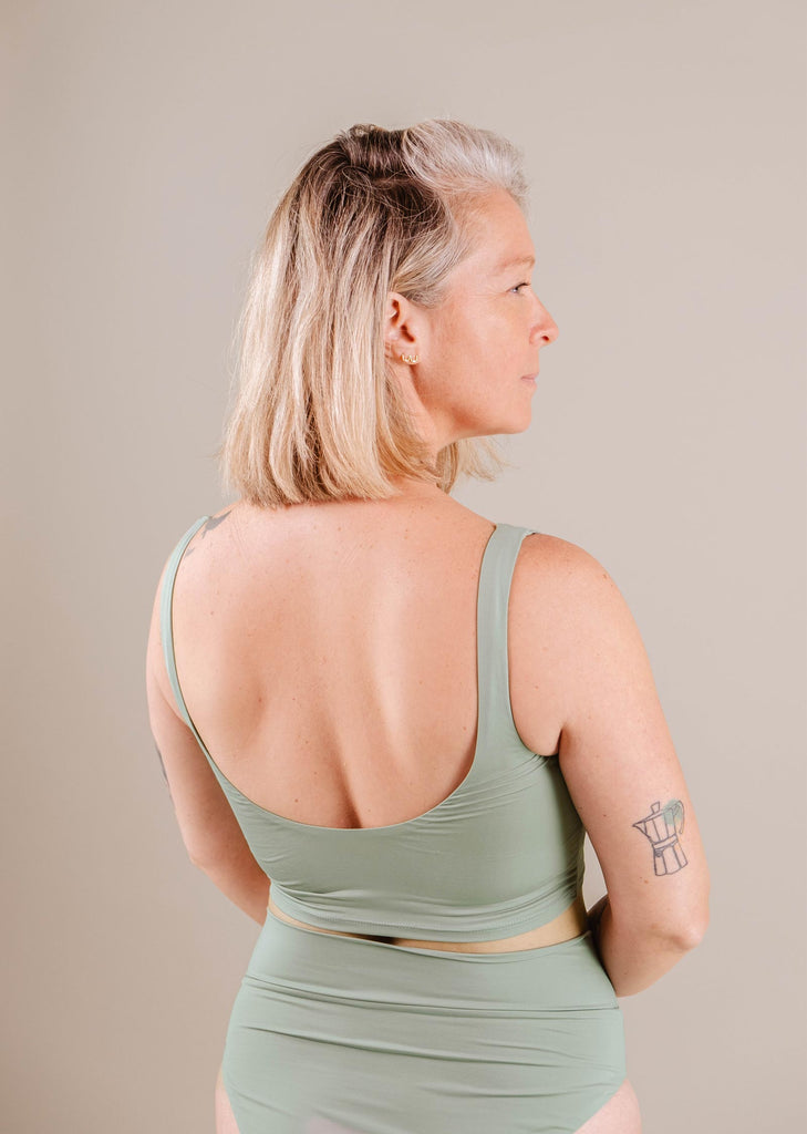 A woman with grey hair seen from the back, wearing a Mimi & August Tahiti Agave Bralette Bikini Top, showing a tattoo on her right upper arm.