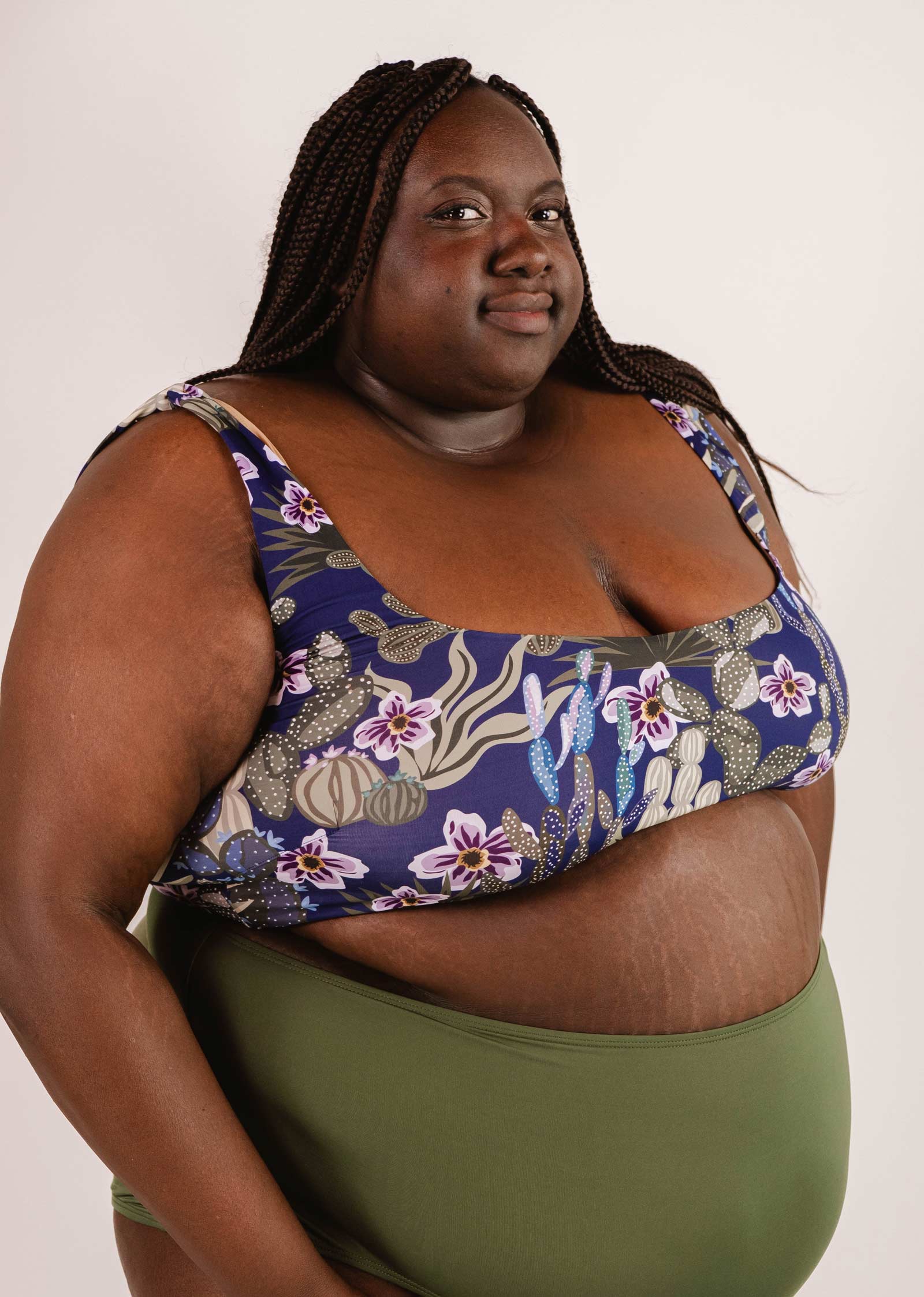 A person with braided hair is wearing the Mimi & August Tahiti Jardin de Nuit Bralette Bikini Top and green bottoms, standing against a plain background.