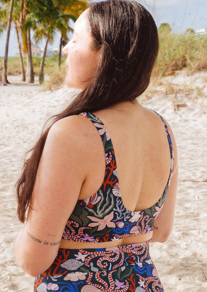 Une femme méditant sur la plage de Mimi et portant le haut de bikini Oceana Tahiti de Mimi et August.
