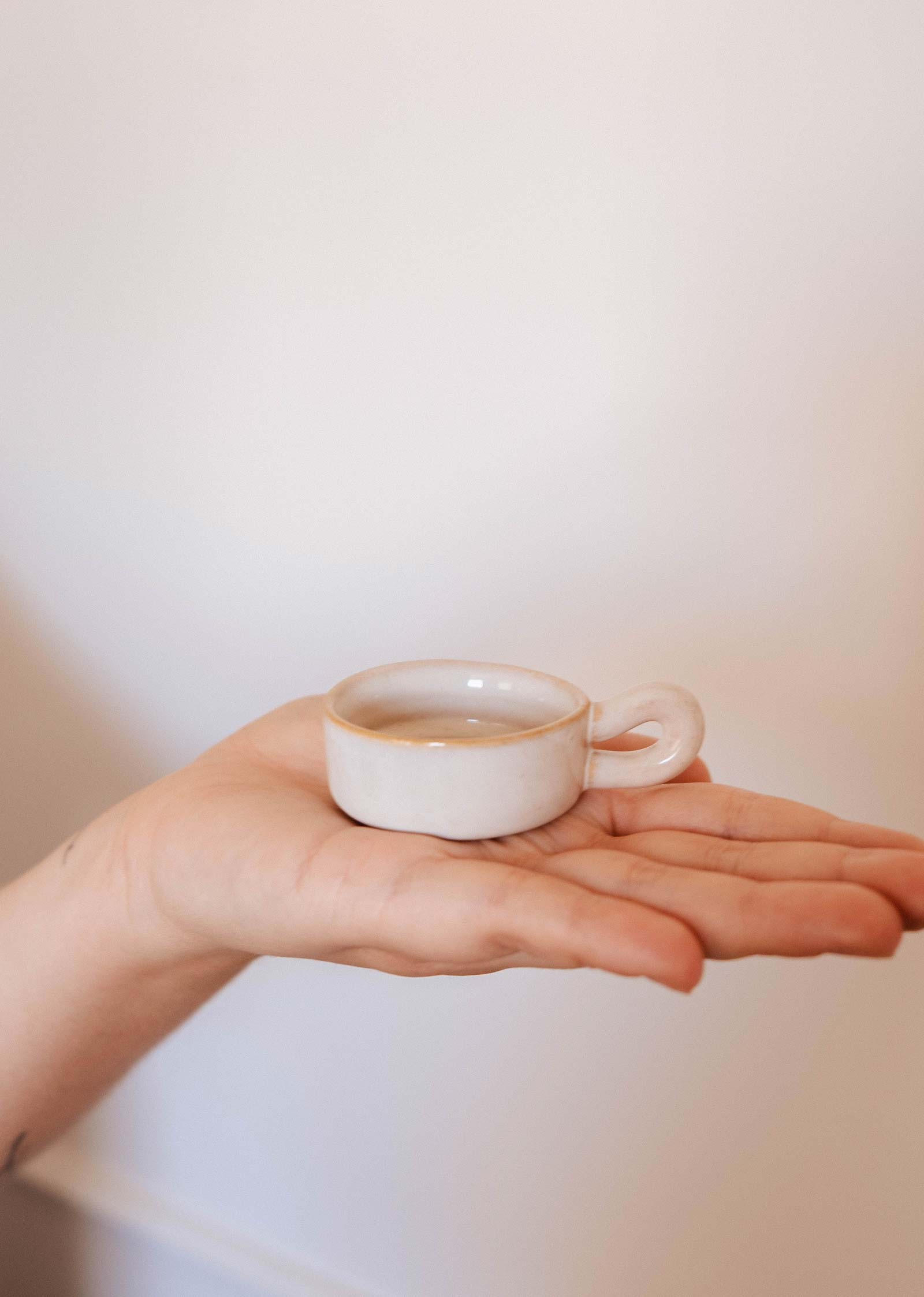 The Mimi & August Tealight Holder, a small white ceramic piece, is displayed on an open palm against a plain background—perfect for adding charm to any rustic decor.