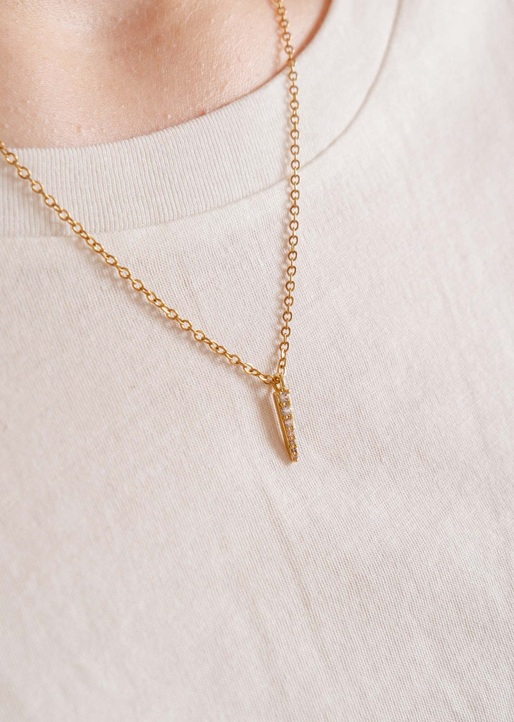 A close up of a person wearing a mimi and august Gold Plated bar-shaped pendant necklace.