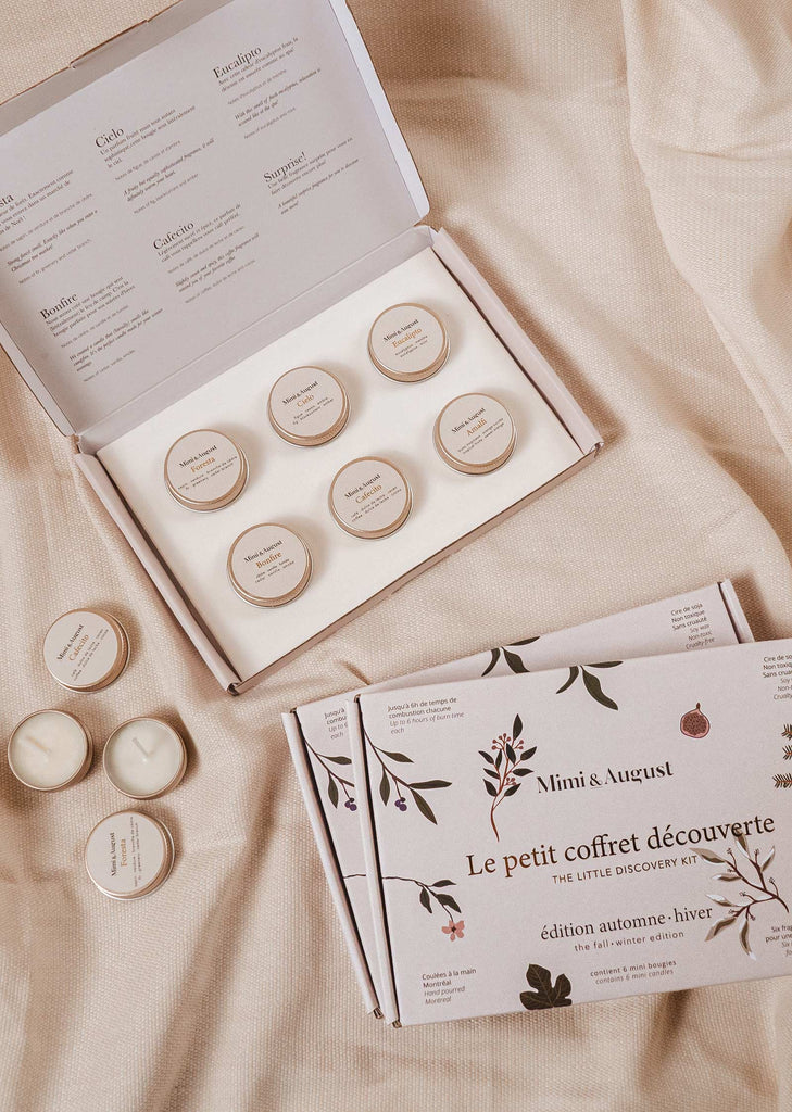 A fall/winter box of cosmetics on a bed, including the Mimi & August Fall/Winter Discovery Kit with various scents.