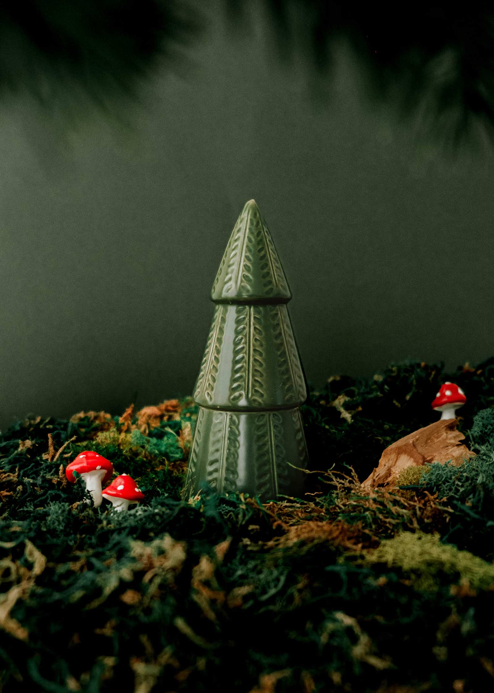 Le sapin vert de Mimi & August est une figurine d'arbre en céramique qui repose sur de la mousse et est entourée de petits ornements en forme de champignons rouges et blancs, ajoutant une touche festive à votre décor de noël.