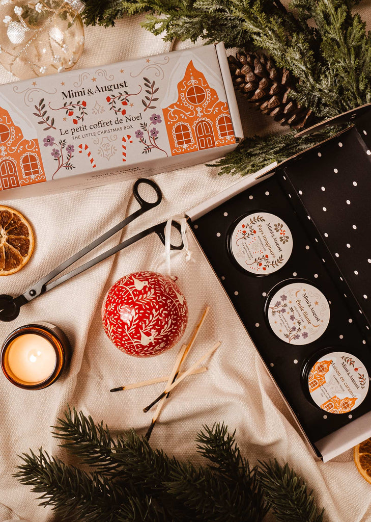 A Mimi & August Little Christmas Box gift set featuring holiday-inspired fragrances in the form of candles and ornaments on a table.