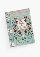 A greeting card titled "The Magic of Christmas" by Mimi & August, featuring floral and vine illustrations on a light blue cover and crafted with recycled paper.