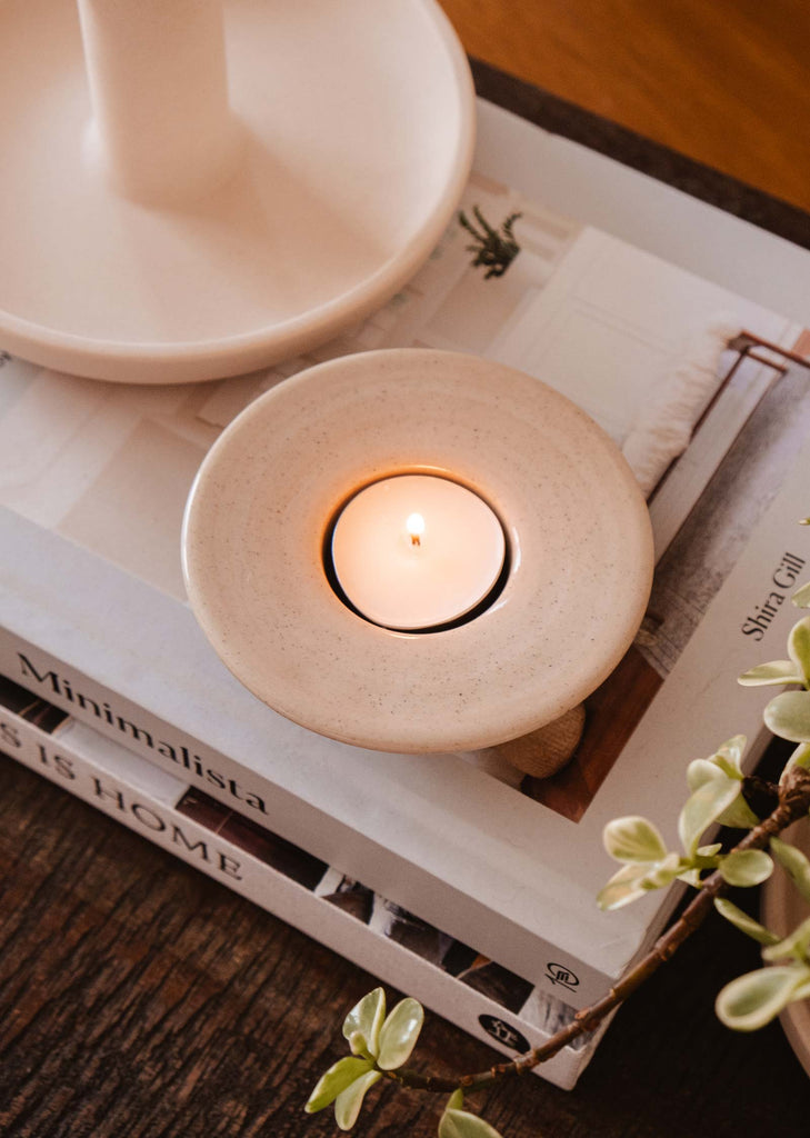 The Round Tealight Holder from Mimi & August sits on top of a book on a table, adding rustic charm to a cozy night's companion.