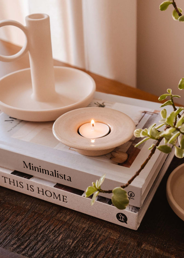 A Mimi & August Round Tealight Holder candle sits on a table next to books, exuding rustic charm.