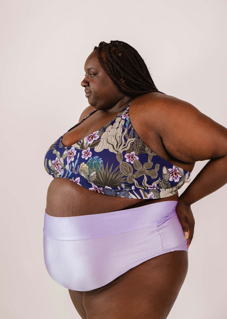 Person wearing a floral-patterned sports bra and Mimi & August Tofino Lilac High Waist Bikini Bottom, posing against a plain background.