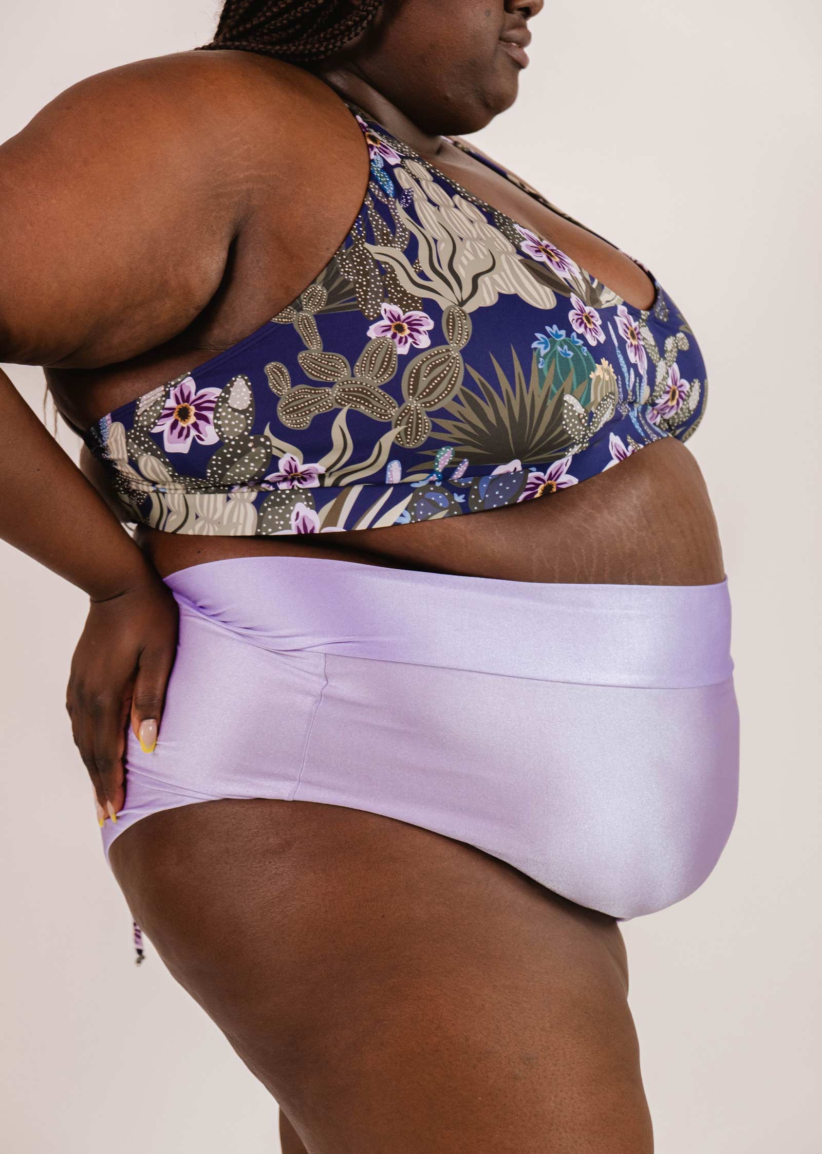 Person shown from the side, wearing a patterned sports bra and Mimi & August Tofino Lilac High Waist Bikini Bottom.