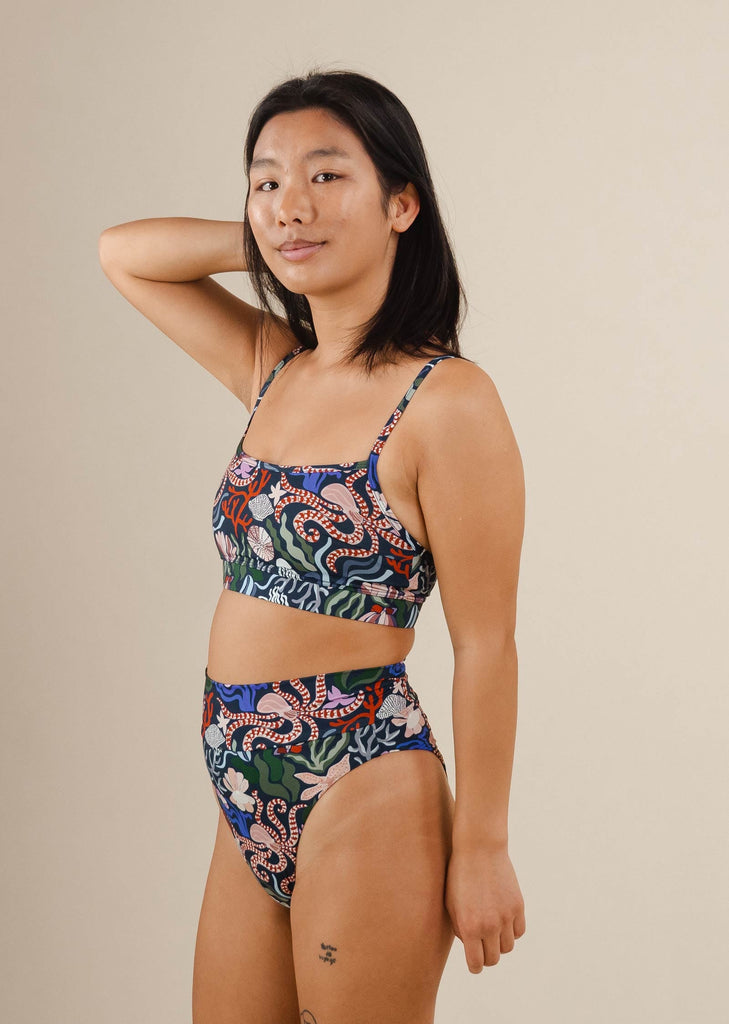 a woman in a patterned marine life swimsuit poses for a picture.