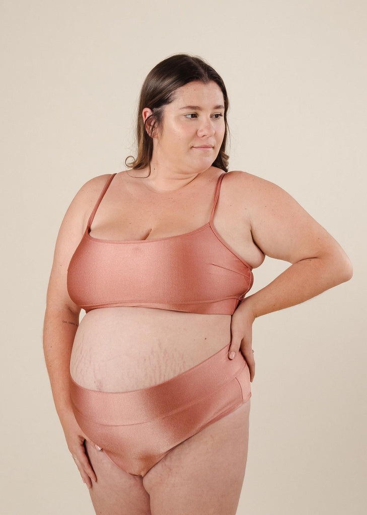 A pregnant woman in a plus-size sustainable pink swimsuit by mimi and august