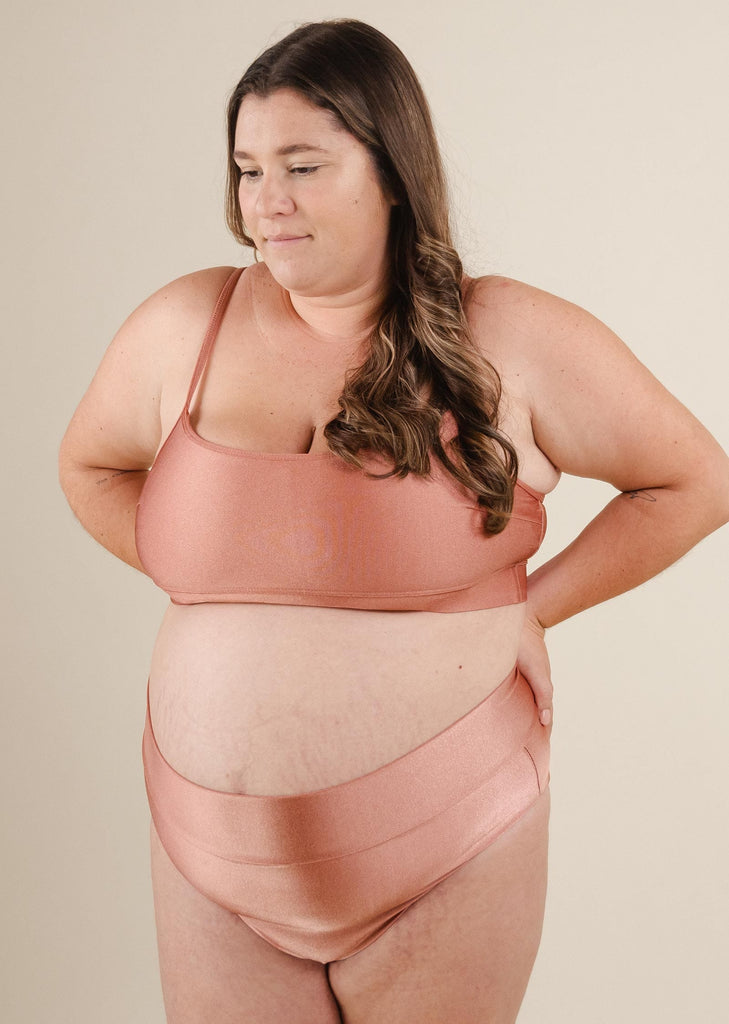 une femme en bikini rose par mimi et august avec les mains sur les hanches.