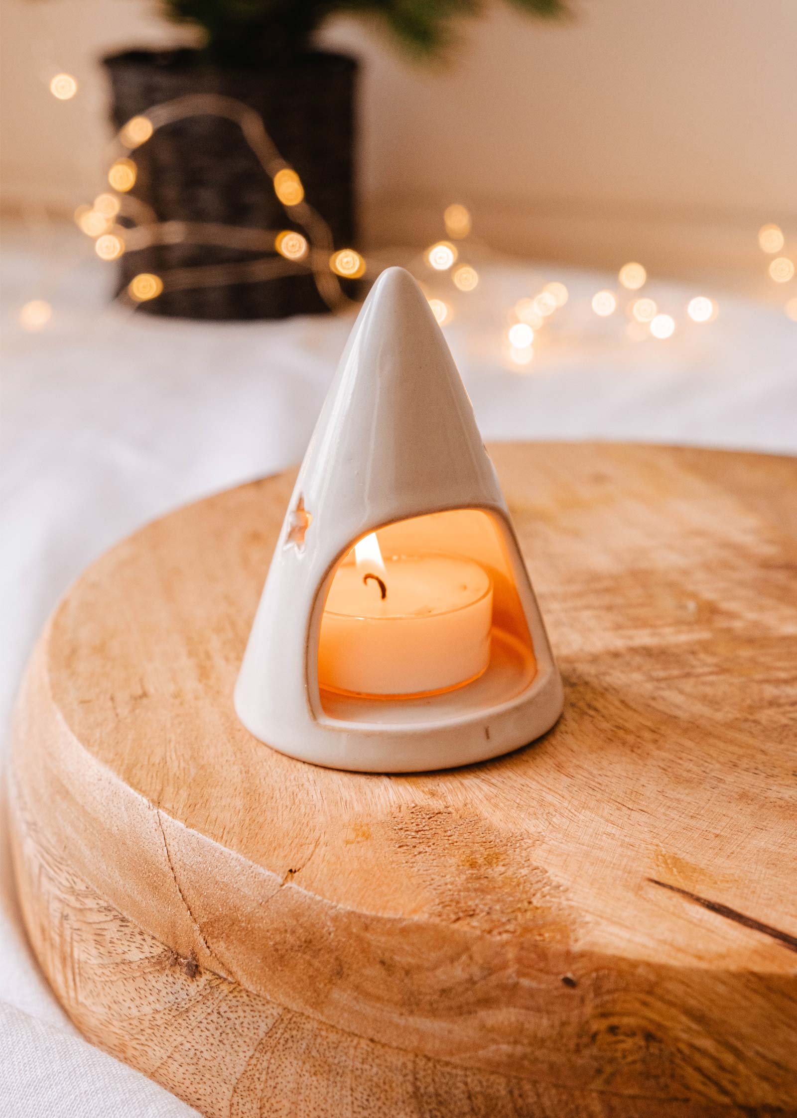 Le Twinkle Tealight Holder de Mimi & August est un charmant bougeoir en céramique conçu en forme de cône avec des découpes en forme d'étoile, idéal pour accueillir une bougie à réchaud incandescente. Posé élégamment sur une surface en bois, avec des lumières de fées qui scintillent doucement en arrière-plan, il constitue une décoration de Noël exquise.