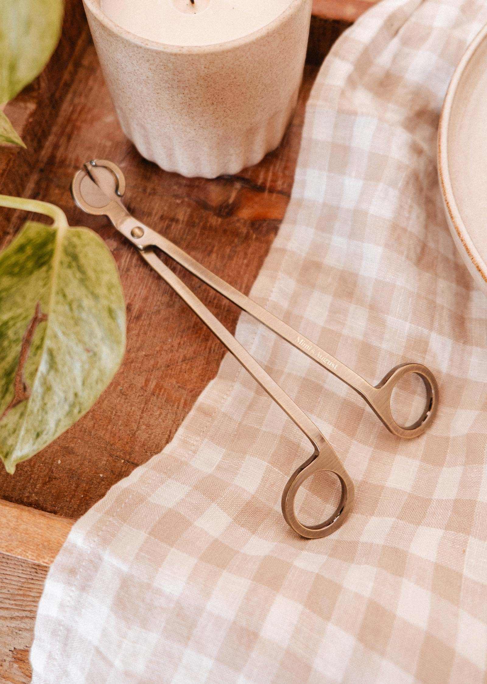 A Mimi & August Wick Trimmer rests on the table, its stainless steel design perfect for trimming candle wicks with ease.