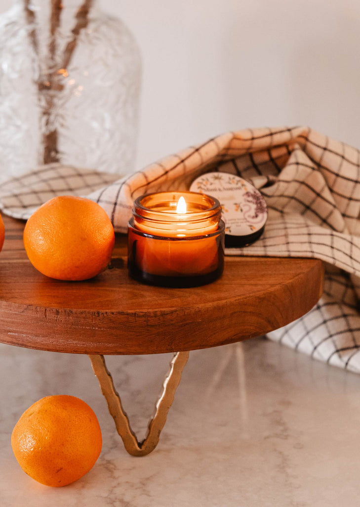 A wooden tray with a Mimi & August Amalfi - Reusable Candle and oranges on it, creating a sensory journey reminiscent of seaside holidays.