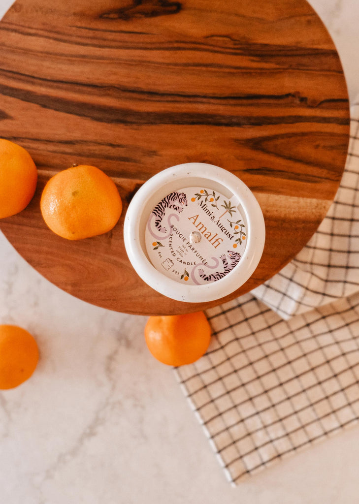 A bowl of oranges on a wooden cutting board, evoking the scents and memories of seaside holidays with the Mimi & August Amalfi - Reusable Candle.