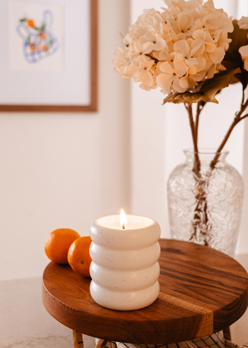 A Mimi & August - Reusable Candle, representing seaside holidays, sits gracefully on top of a wooden board, transporting you on a sensory journey of tranquility.