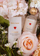 La Bruine d’ambiance Amore Mimi & August, mise en scène avec des fleurs roses et blanches ainsi qu’une verdure luxuriante, diffuse un parfum floral tout en douceur et instaure une atmosphère romantique et apaisante.
