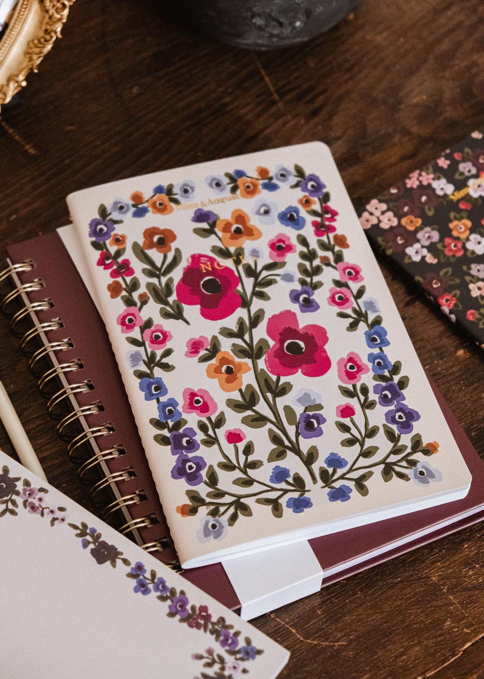 Bouquet floral notebook by Mimi & August resting on a spiral notebook with a pen and a floral accessory on a wooden surface.