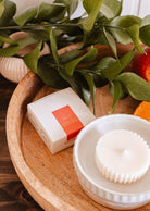 The Mimi & August Candle Refill - Amalfi, crafted from natural soy wax, sits on a tray beside its box and green leaves, evoking a fresh Mediterranean fragrance.
