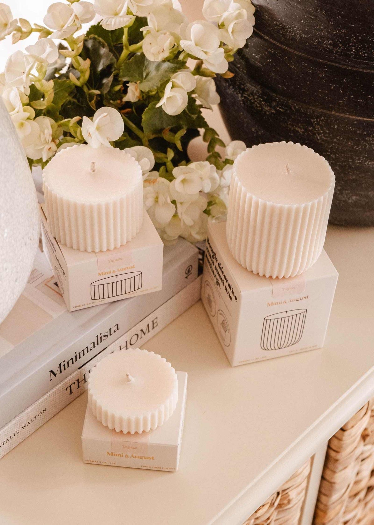 Three ribbed cream Candle Refill Topaze by Mimi & August sit on white boxes next to white flowers and stacked books, filling the space with a warm sandalwood coconut vanilla aroma.