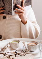 Le Petit Café Mimi – Two Little Cups Candle Set mugs filled with wax sitting on a table in front of a person reading a book.