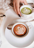 Le Petit Café Mimi – Two Little Cups Candle Set featuring two small ceramic cups on saucers, one holding a latte art candle and the other holding a green matcha latte.